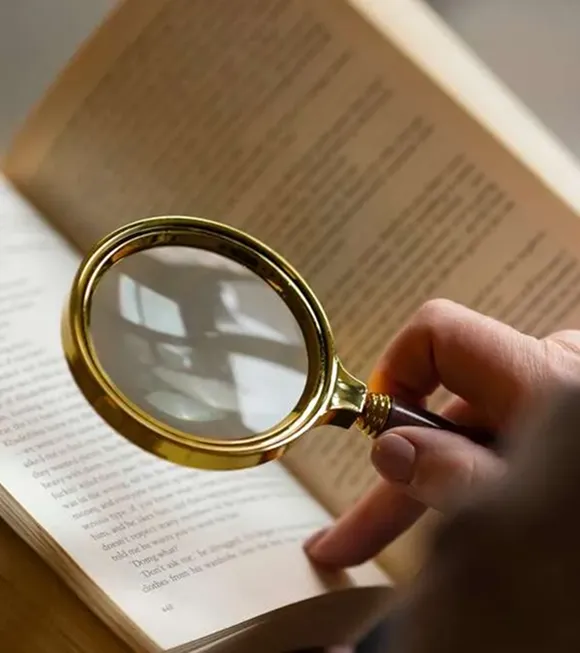 A person studies a book with a magnifying glass, focusing on the details of the text.