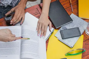 A group of people gathered around a table, engaged with books and various items spread out before them.