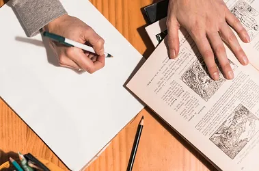 A person writes in a book with a pen, focusing intently on their task.